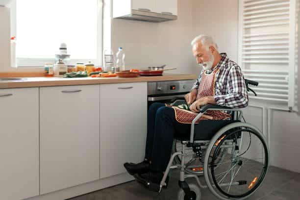 Disabled senior man in a wheelchair preparing food in the kitchen